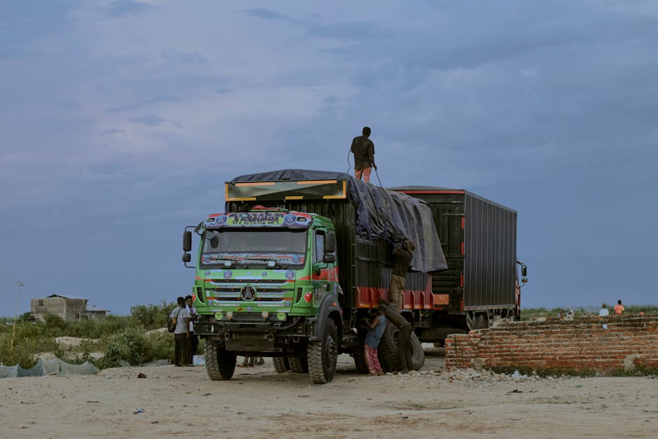 A vibrant truck with workers loading cargo in an outdoor setting under a cloudy sky.